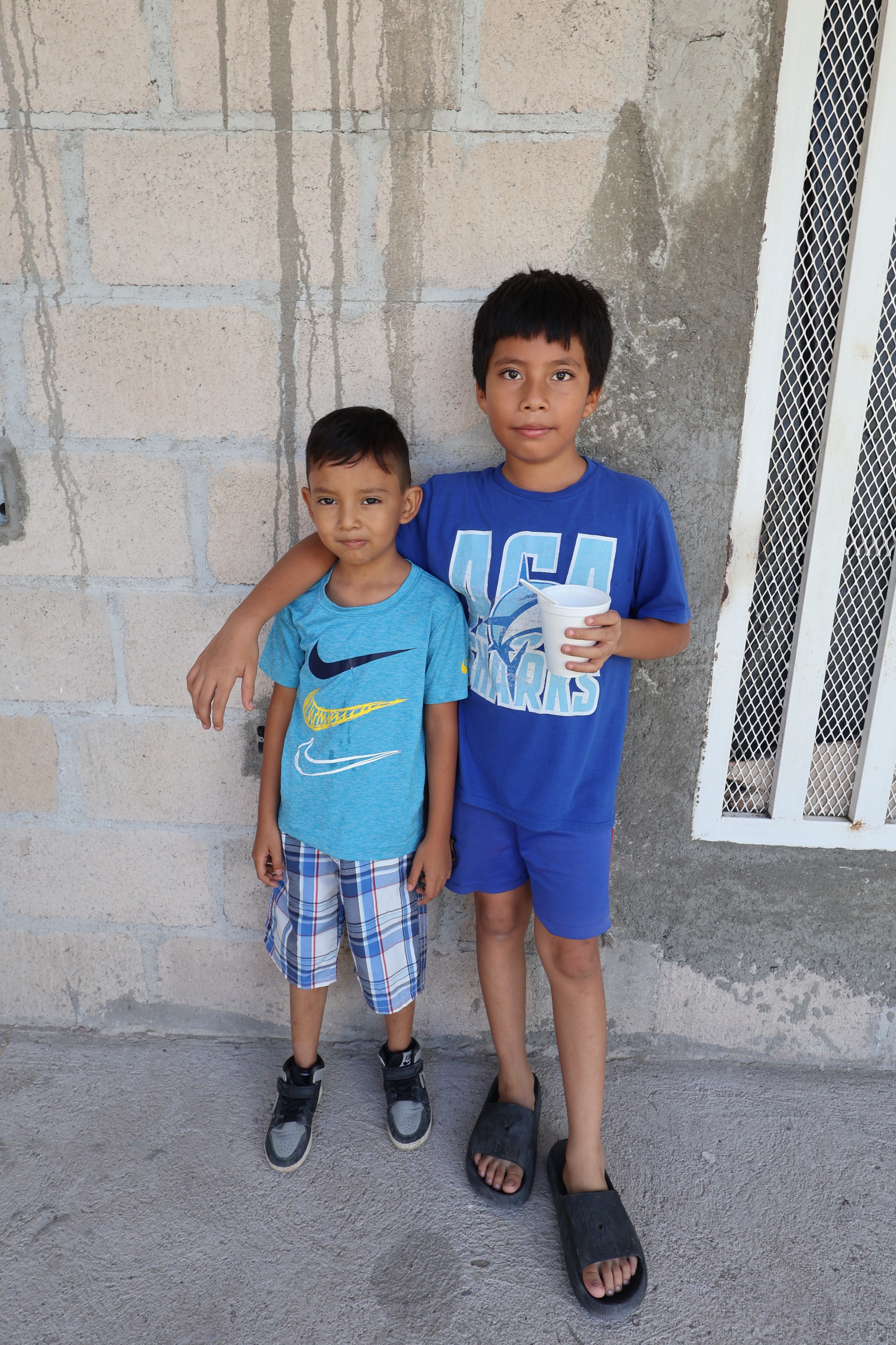 Two young boys posing against a concrete wall