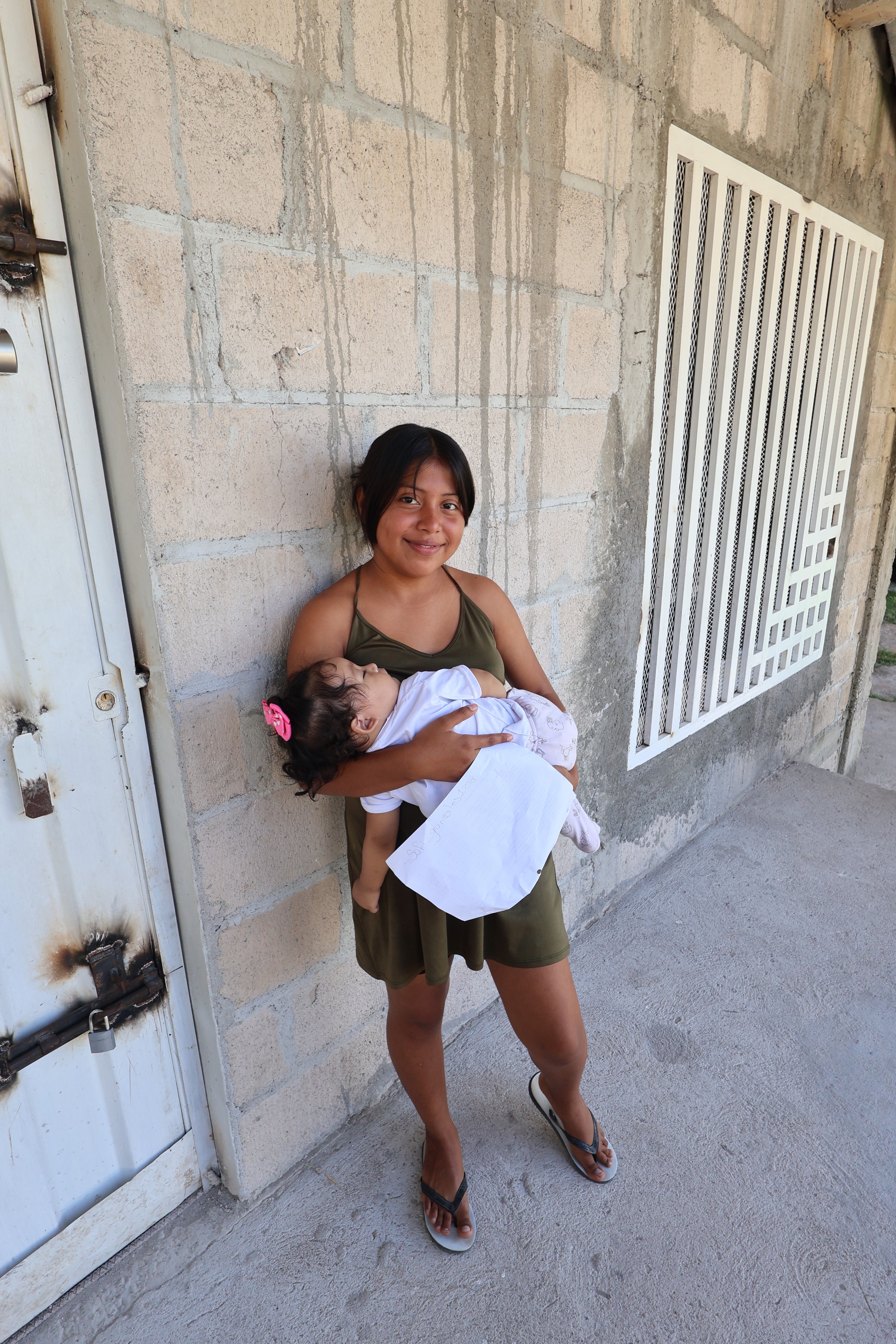 Woman holding an infant against a concrete wall